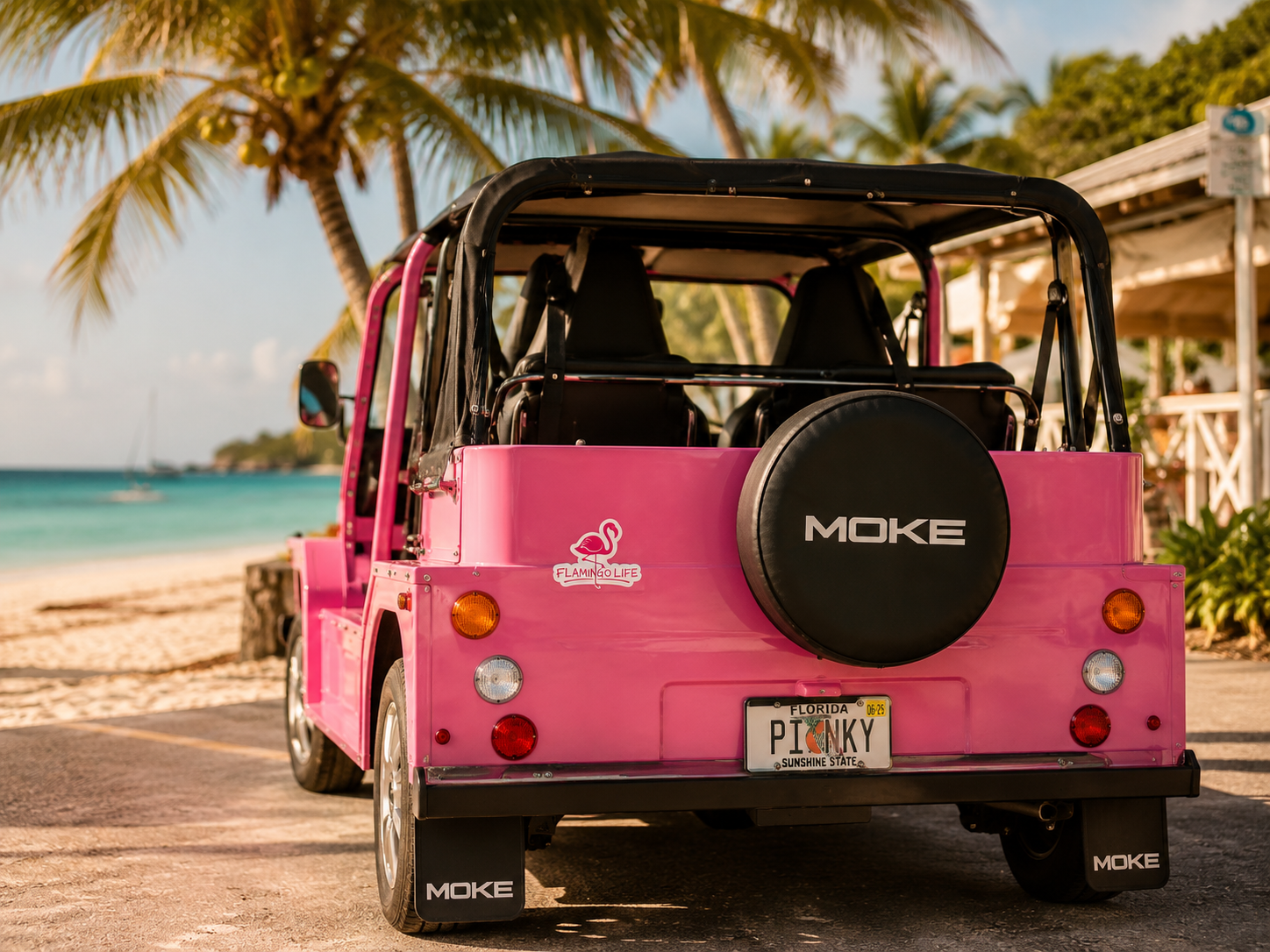 Pink Moke vehicle with Flamingo Life decal on a beach with palm trees and ocean in the background.